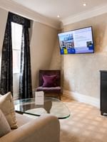 Elegant living area with couch, chair, glass table, and TV in the Townhouse Junior Suite at The Capital Hotel London.
