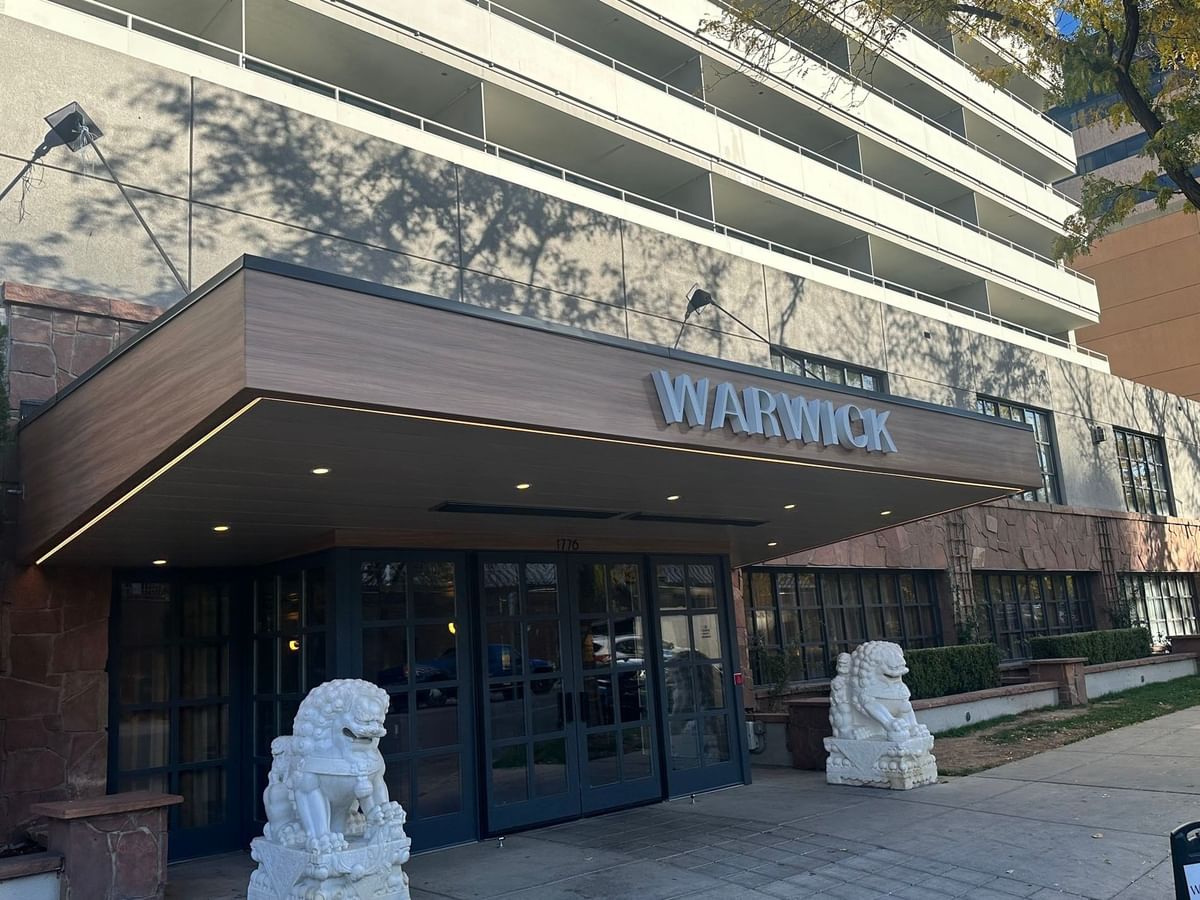 White stone lions guard the Warwick Denver entrance near the wooden awning and glass doors