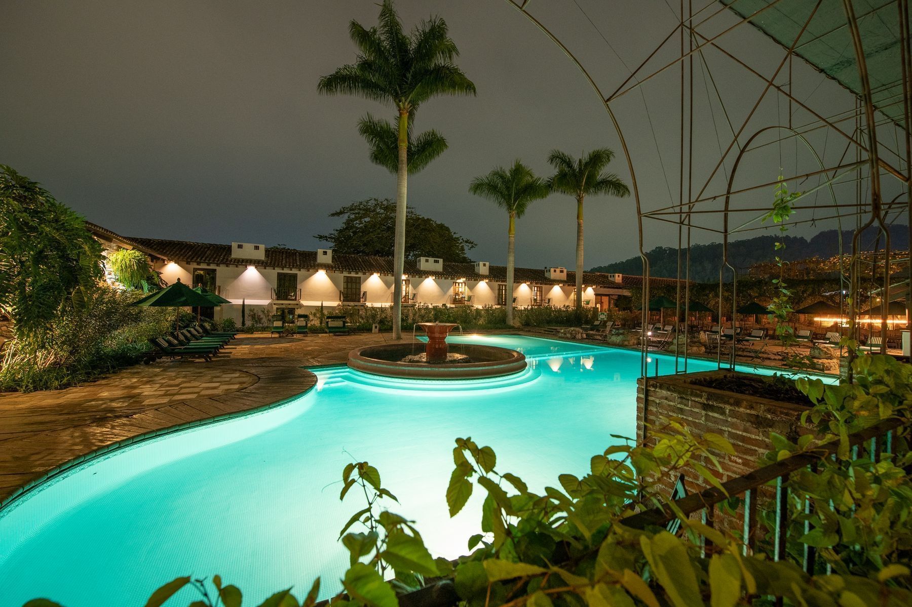 Piscina iluminada con una luz azul brillante, con palmeras bajo el cielo nocturno en Casa Santo Domingo