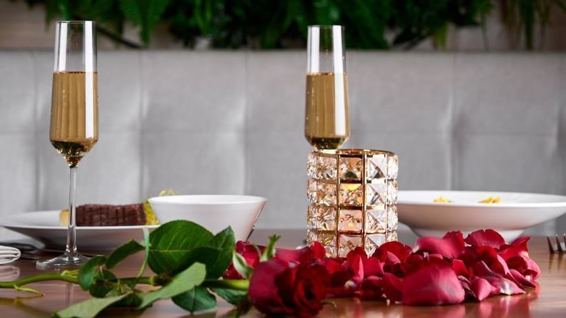 Intimate dining setup with champagne flutes, an elegant candle and red roses on a wooden table at Paramount Hotel Dubai