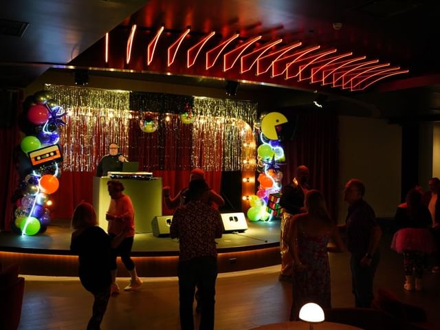 Stage with red lights, DJ and people dancing.