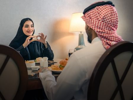 Couple enjoying in-room dining with a burger and fries at Saja by Warwick Makkah.