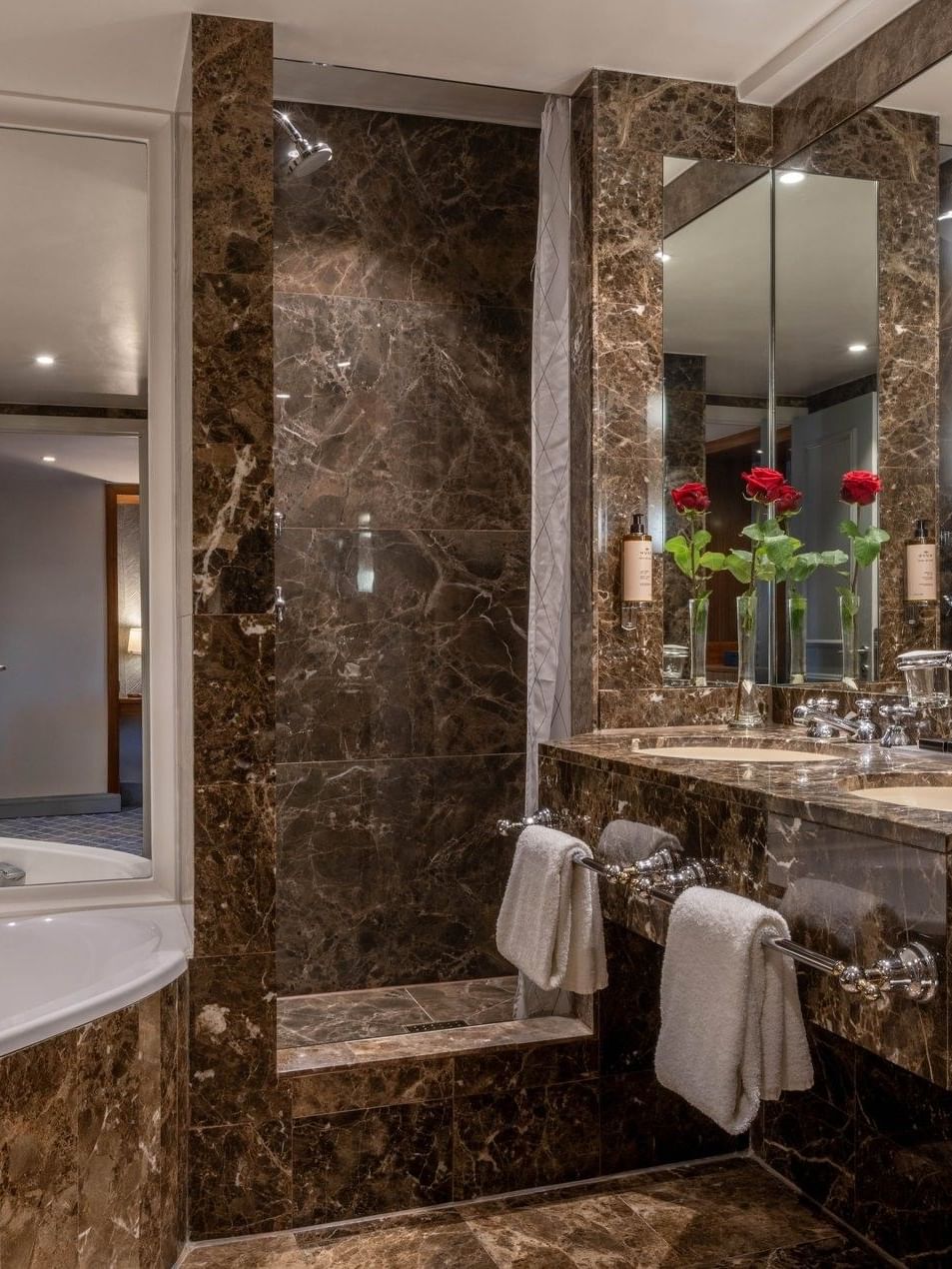 Premium Deluxe Room bathroom featuring sink with roses in vases by wall mirrors and bathtub at Warwick Grand Place Brussels
