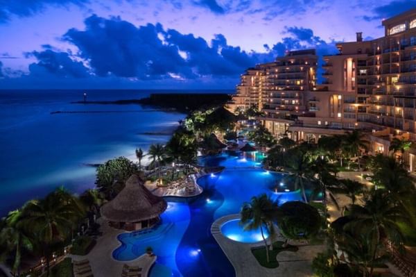 Aerial view of pool, palm trees & exterior of hotel at night at Fiesta Americana Travelty