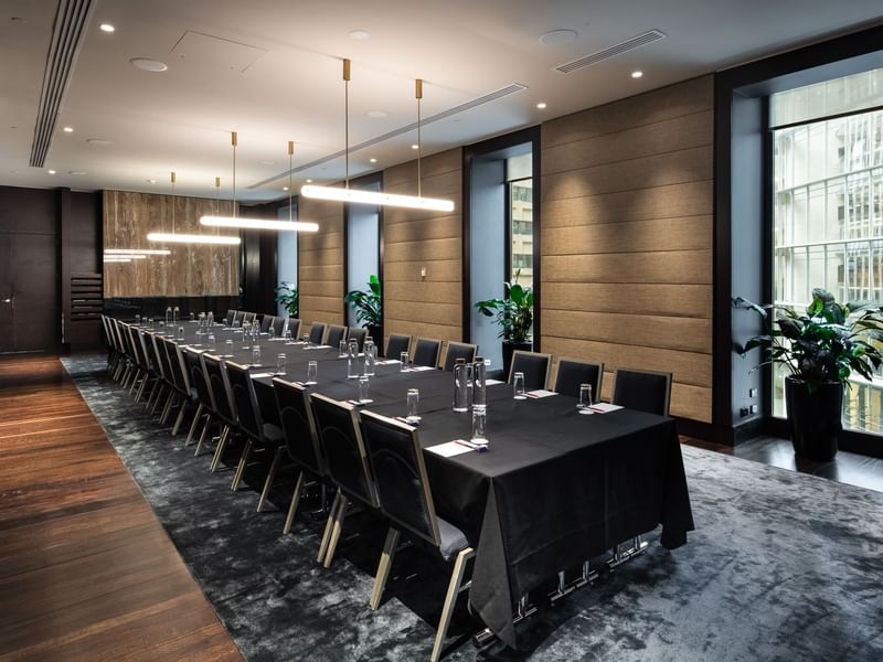 Long table with black chairs, black tablecloth, and water glasses, surrounded by a modern conference room.