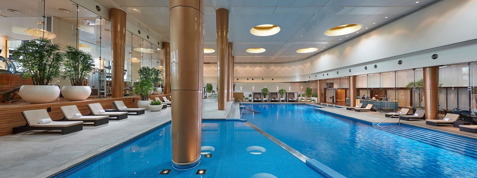 Indoor pool with lounge chairs, circular lights overhead, and large windows at Crown Hotel Melbourne