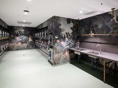 Laundry room with white floors, wall art, and sinks, with several washing machines.