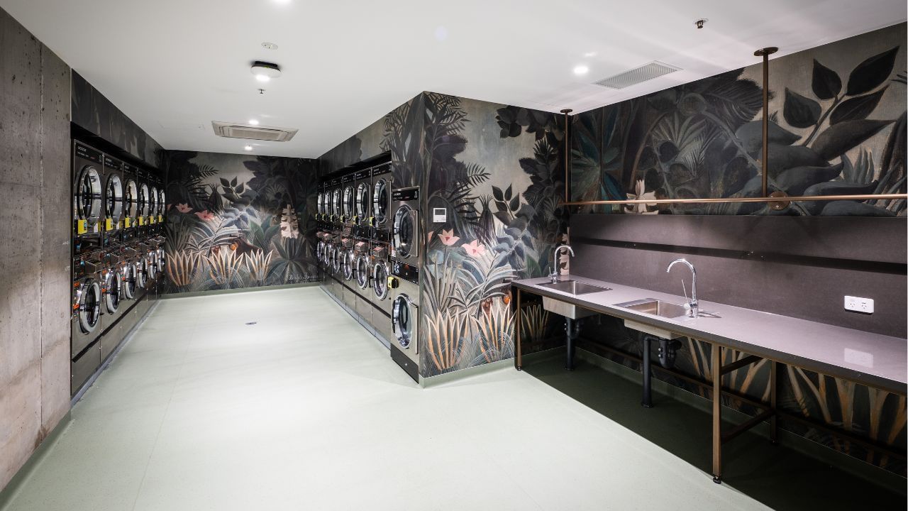 Laundry room with white floors, wall art, and sinks, with several washing machines.