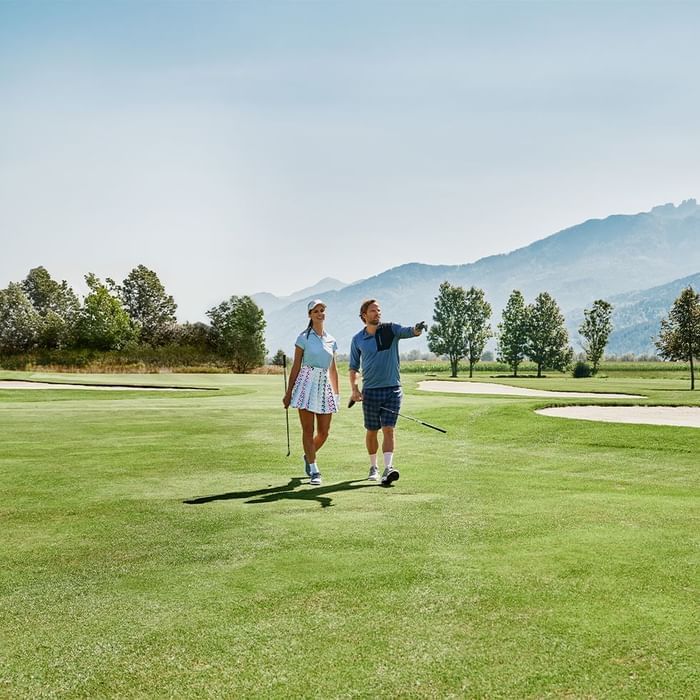 Par igra golf na golf terenu s planinama u pozadini.