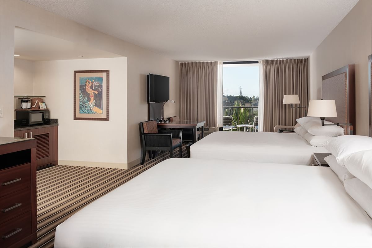 A hotel room with two queen beds, a desk, TV, and window with a view.