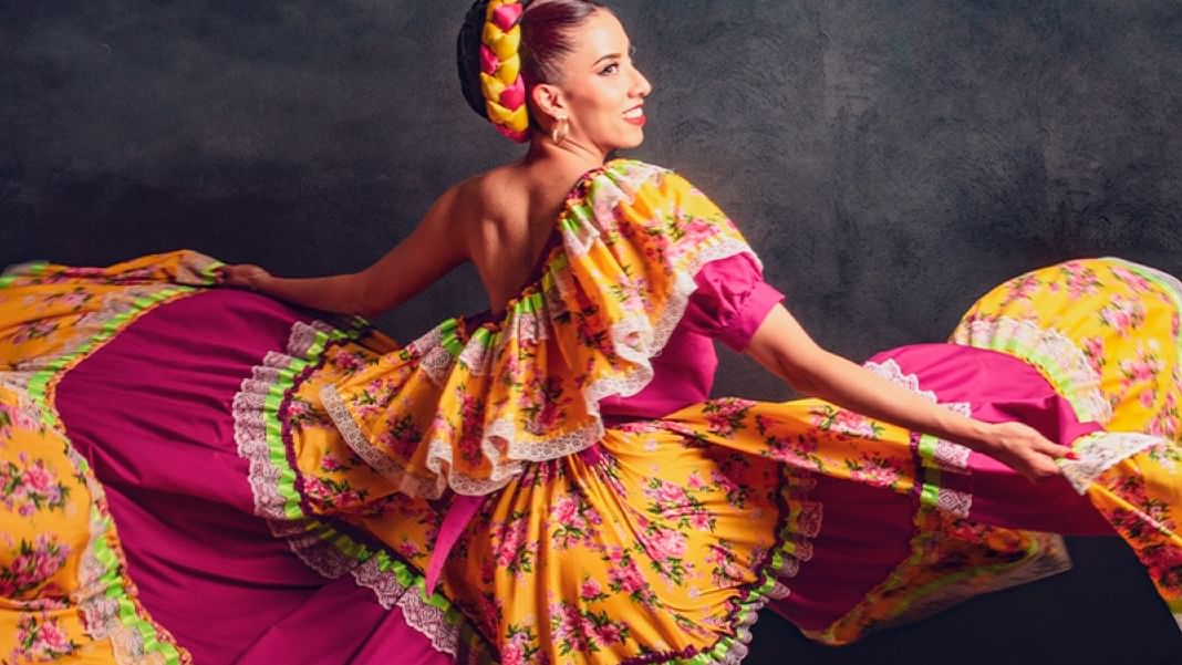 Dancer in vibrant traditional Mexican dress with colorful floral patterns twirling against a dark backdrop.