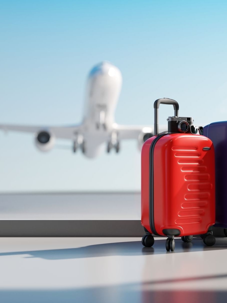 Red and purple suitcases placed by a large window with a plane in the sky at Warwick Grand Place Brussels