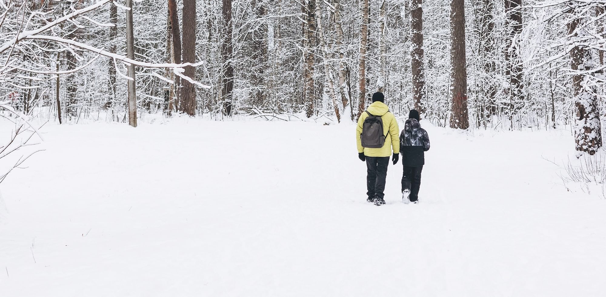 Two people wearing backpacks walk through a snowy forest with snow-covered trees at Coast Calgary Universit