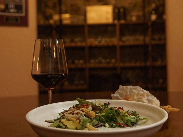 Glass of red wine and a salad on a white plate in La Cava de Santiago restaurant at Hacienda del Mar Los Cabos.