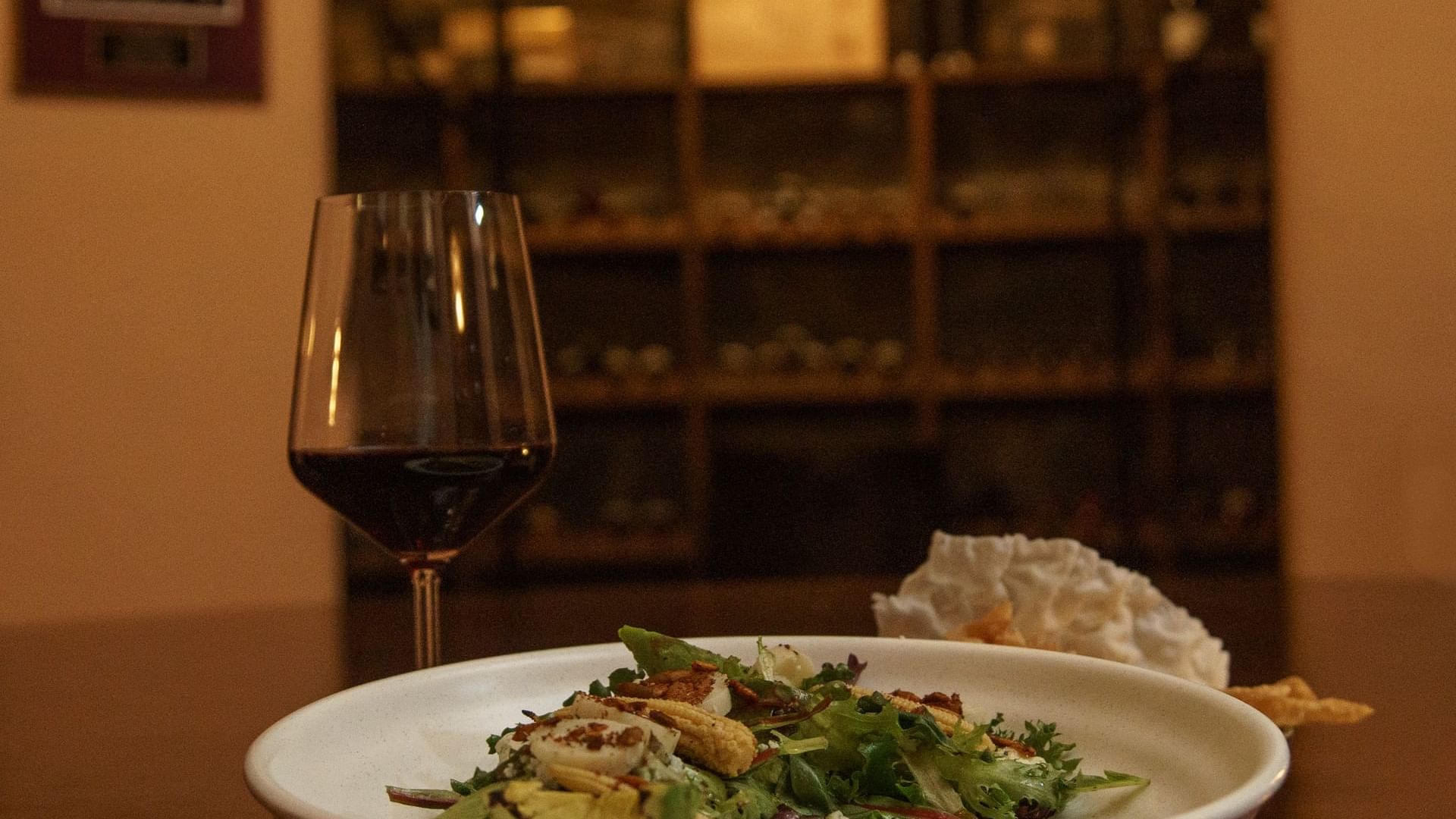 Glass of red wine and a salad on a white plate in La Cava de Santiago restaurant at Hacienda del Mar Los Cabos.