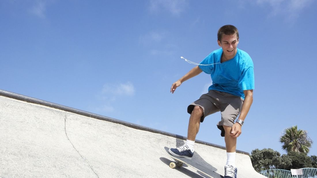 Young skateboarder in blue shirt performing trick on concrete ramp at Haslams Pump Track under clear blue sky.