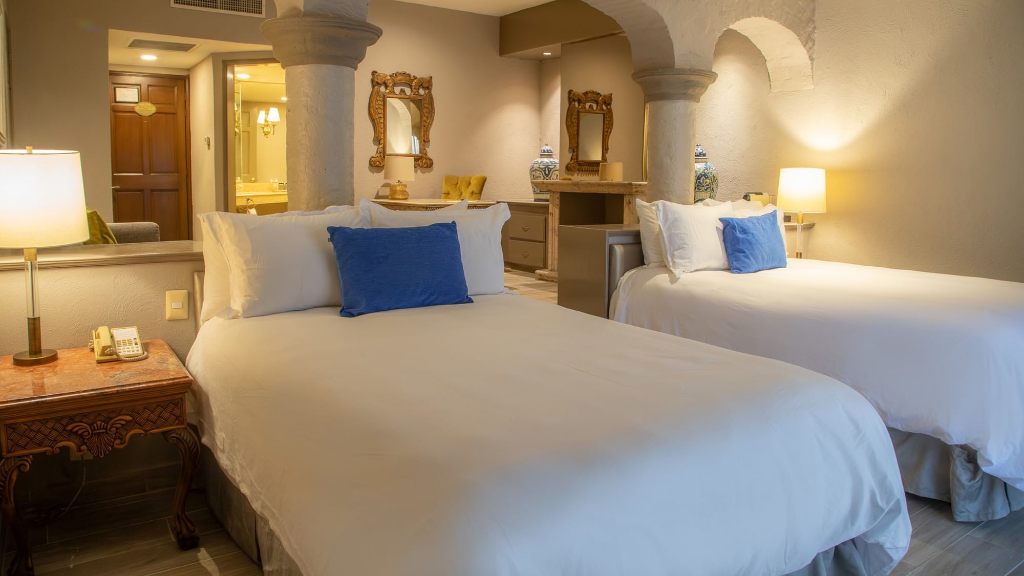 Habitación elegante con dos camas dobles, ropa blanca, cojines azules y arcos coloniales en Quinta Real Guadalajara