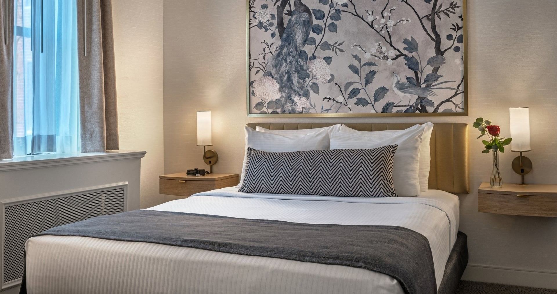 King bed with white sheets and gray blanket, nightstands with lamps and vase, peacock wall art at Warwick Allerton Chicago