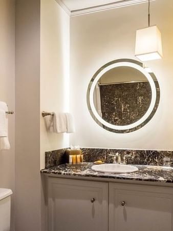 Backlit round mirror by a marble vanity under a pendant lamp in Superior Queen Room at Warwick San Francisco