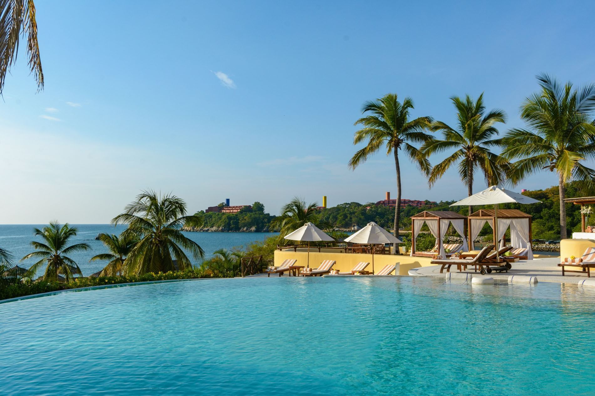 Aerial view of Quinta Real Huatulco featuring white domes by a pool surrounded by thatched roofs at the coast