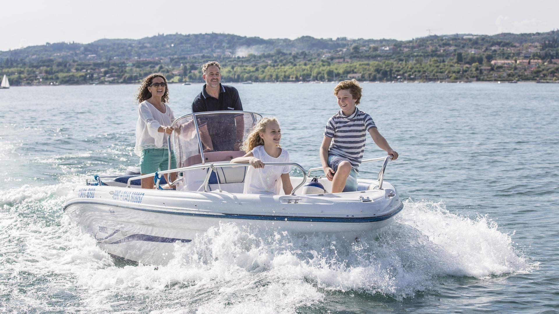 A family of four on a motorboat on a lake with hills in the background.
