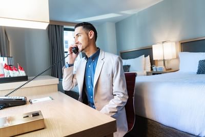 Guest using a desk phone beside two white beds under glowing bedside lamps in a bright guest room at Hotel Saint Clair