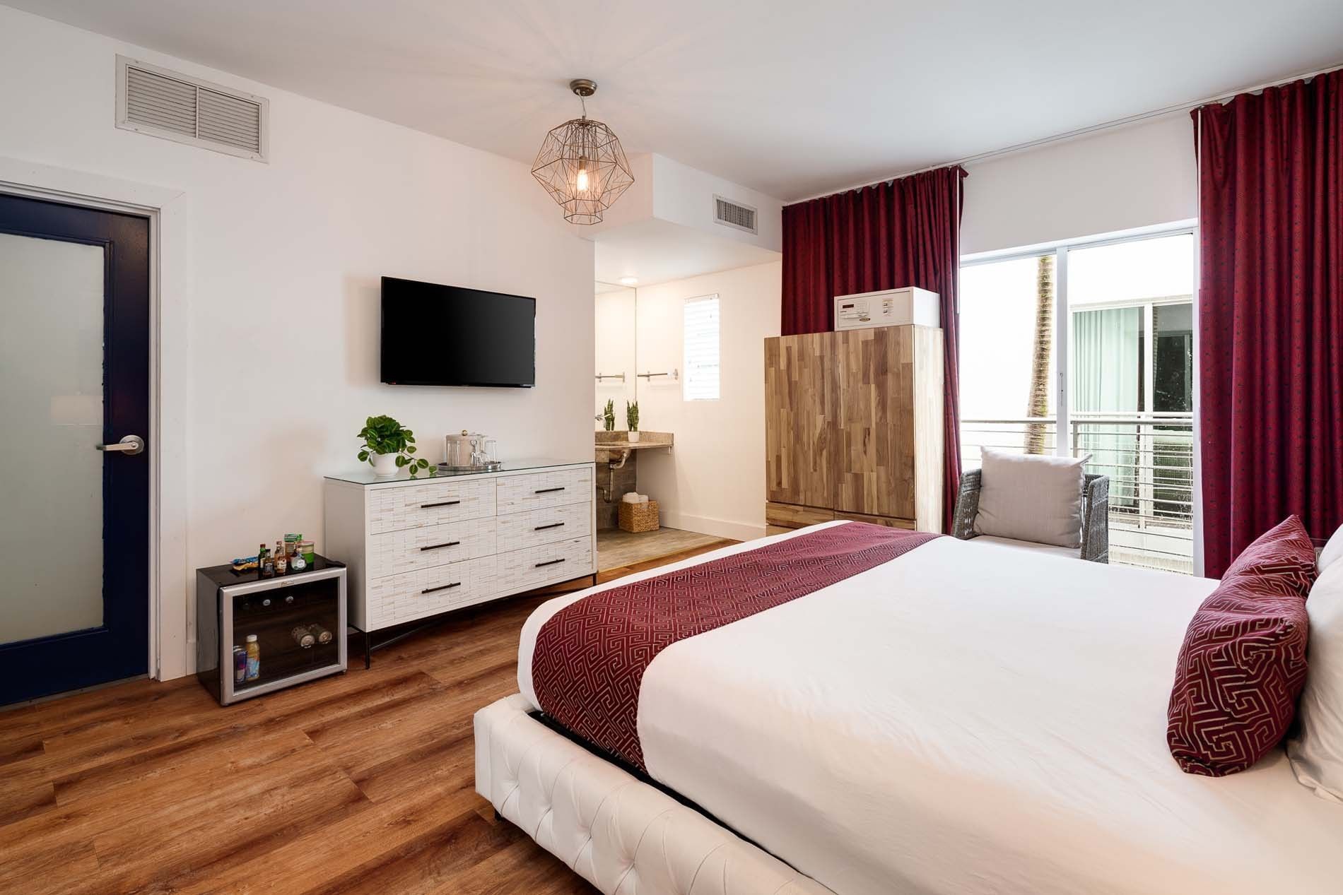 A hotel room with a large bed, dresser, TV, and balcony