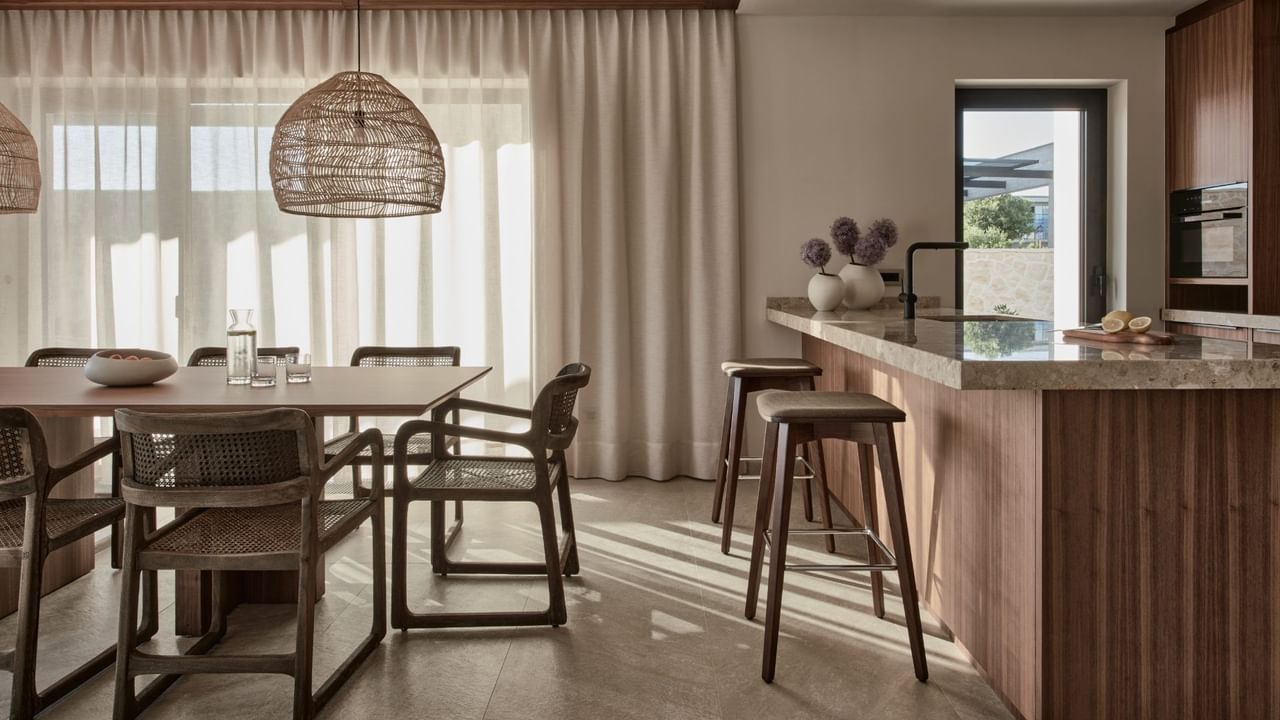 Kitchen interior with a dining table, chairs, bar stools, and a wicker pendant lamp at Falkensteiner Luxury Villas