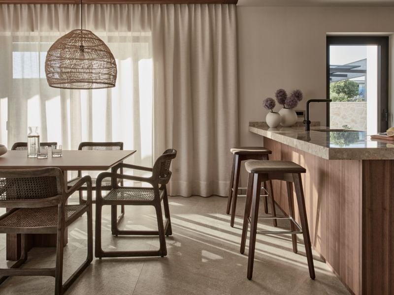 Kitchen interior with a dining table, chairs, bar stools, and a wicker pendant lamp at Falkensteiner Luxury Villas