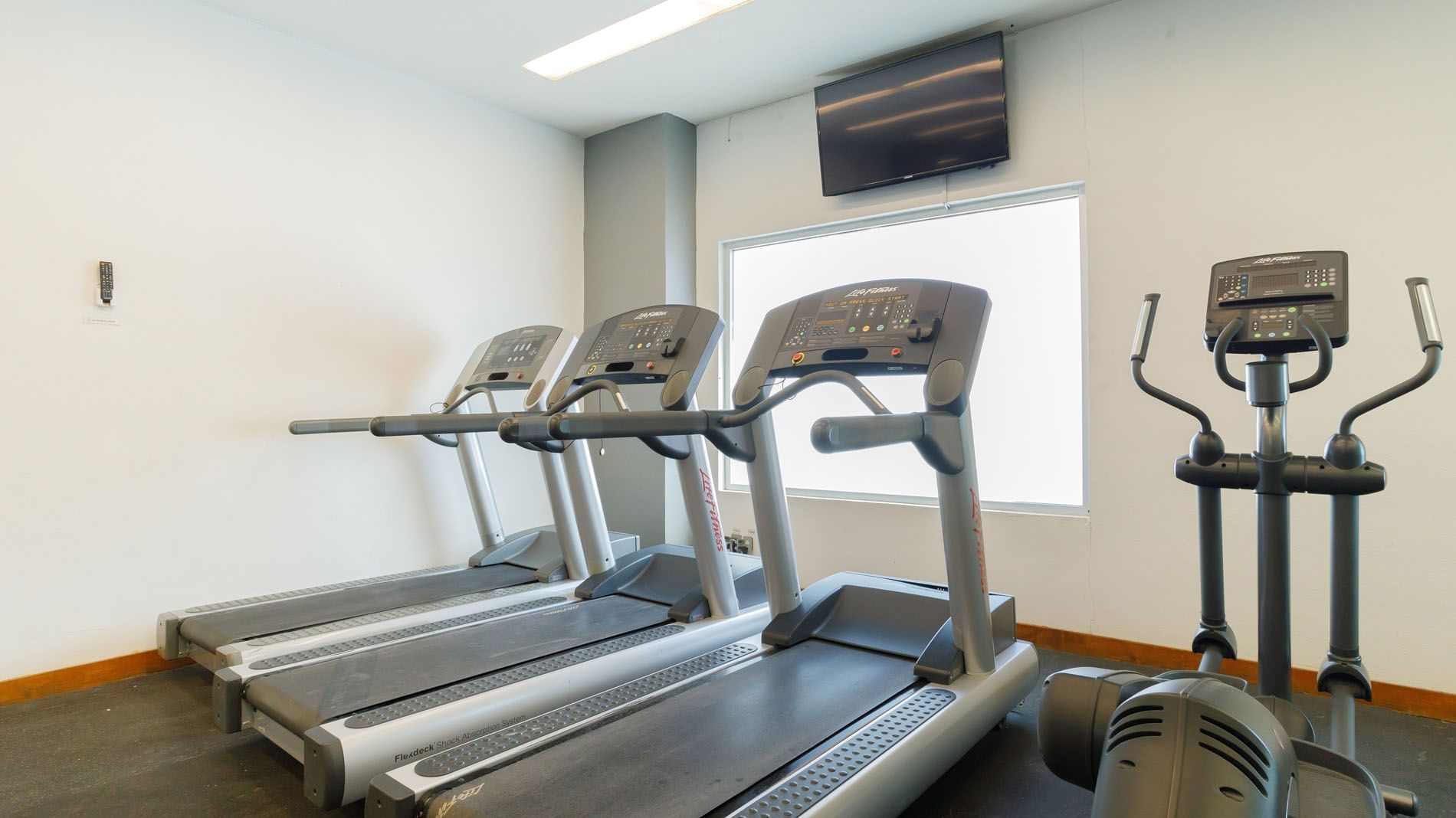 Modern cardio room featuring professional treadmills and an elliptical near a large window at Real Inn Torreon