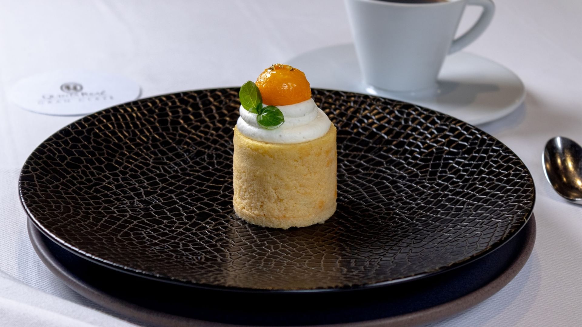 Small gourmet dessert with cream and orange fruit on a black textured plate at Quinta Real Oaxaca