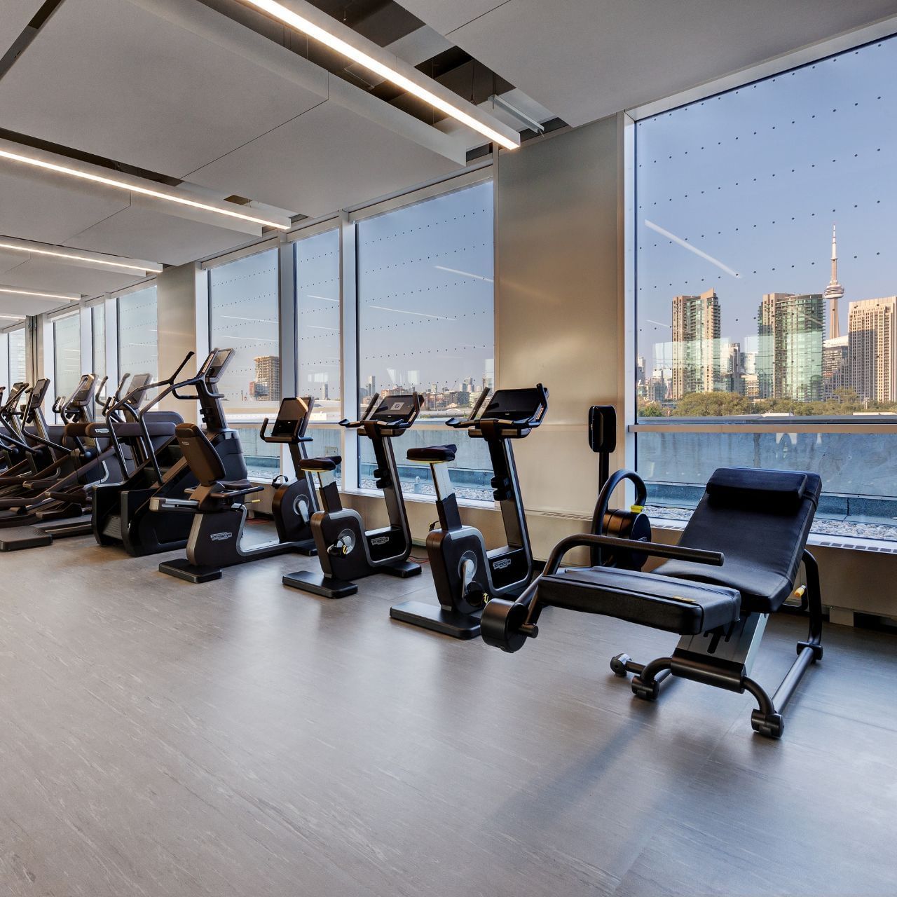 Fitness centre with exercise bikes and training equipment by skyline-view windows at Hotel X Toronto