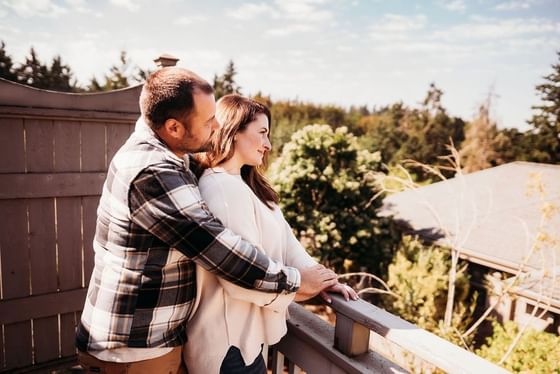 Man hugging a woman by a wooden deck railing under a soft blue sky with light clouds at Oregon Garden Resort