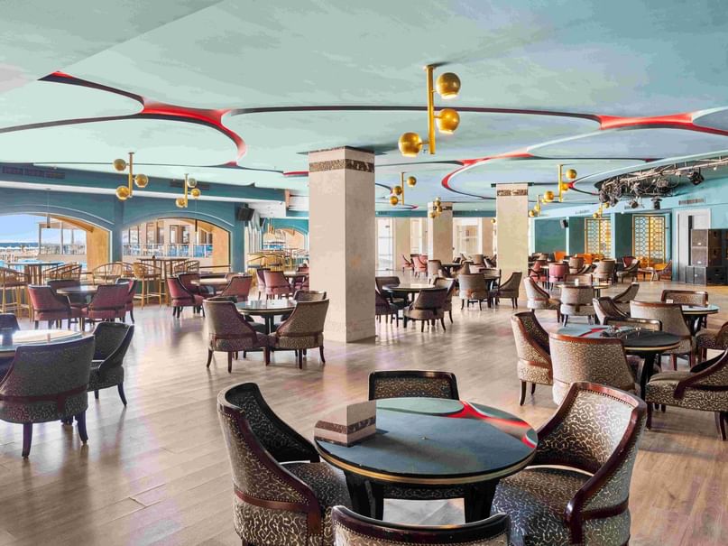 An elegant Lounge Bar with wooden floors, round tables, and leopard print chairs under a decorative ceiling.