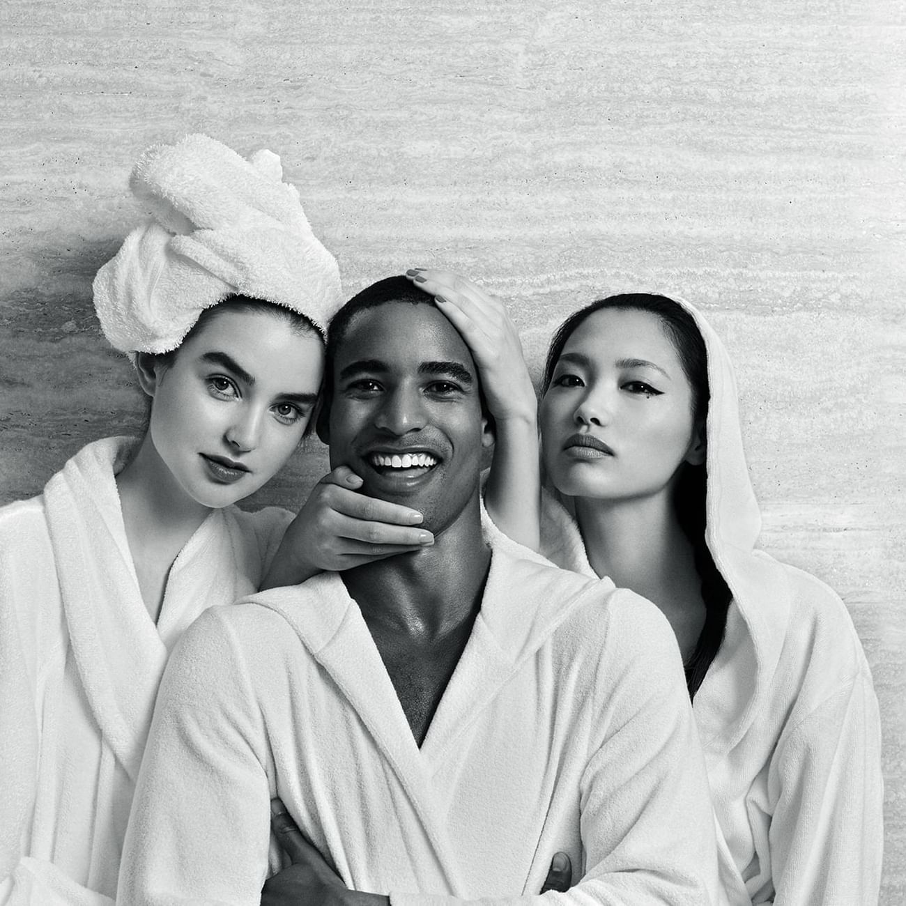 Black & white image of three individuals in bathrobes smiling and posing together at Sofitel Brisbane Central