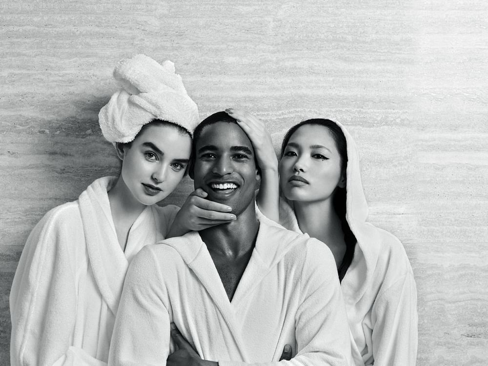 Black & white image of three individuals in bathrobes smiling and posing together at Sofitel Brisbane Central