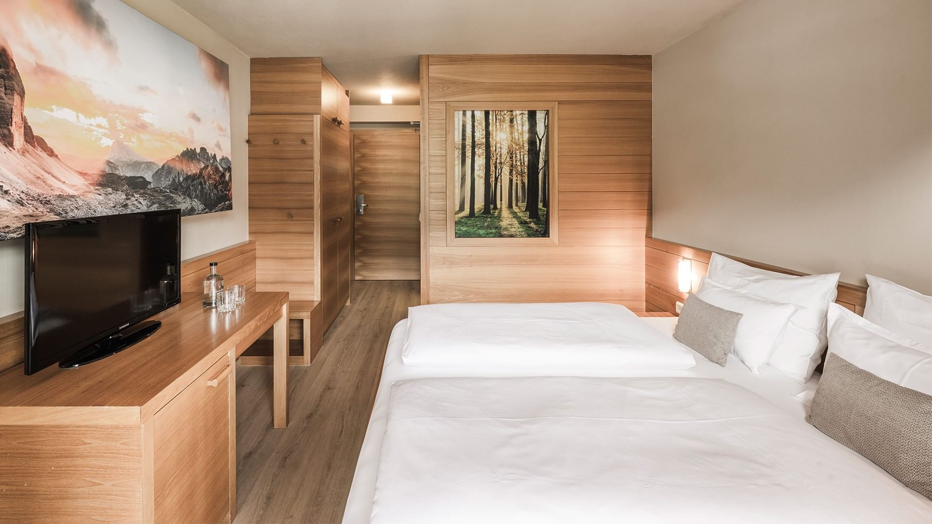 Camera d'albergo moderna con due letti, TV, e decorazioni naturali sulle pareti.