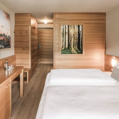 Interior of a hotel room with wooden furniture, two beds, TV, and scenic wall art.