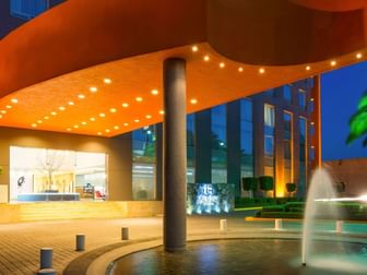 Illuminated entrance featuring a bright orange canopy, water fountain, and modern design at Real Inn Perinorte