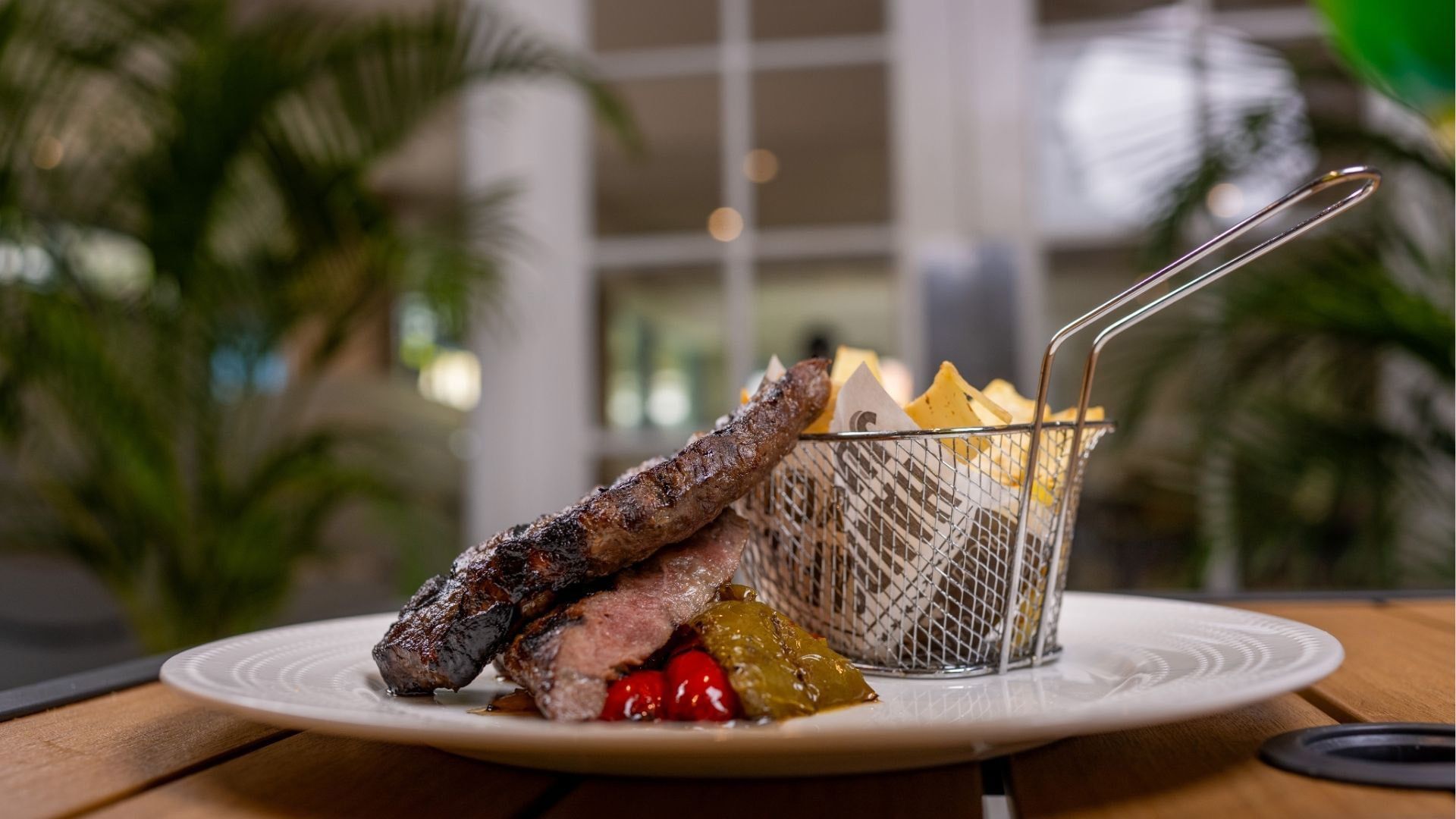 Juicy sliced steak on a white plate, by a wire basket of fries under a leafy canopy in Meet the Chef at Time Out Hotel
