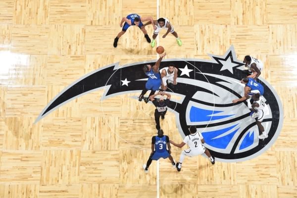 An aerial shot of the Kia Center court with the Orlando Magic logo and several players mid-game. 