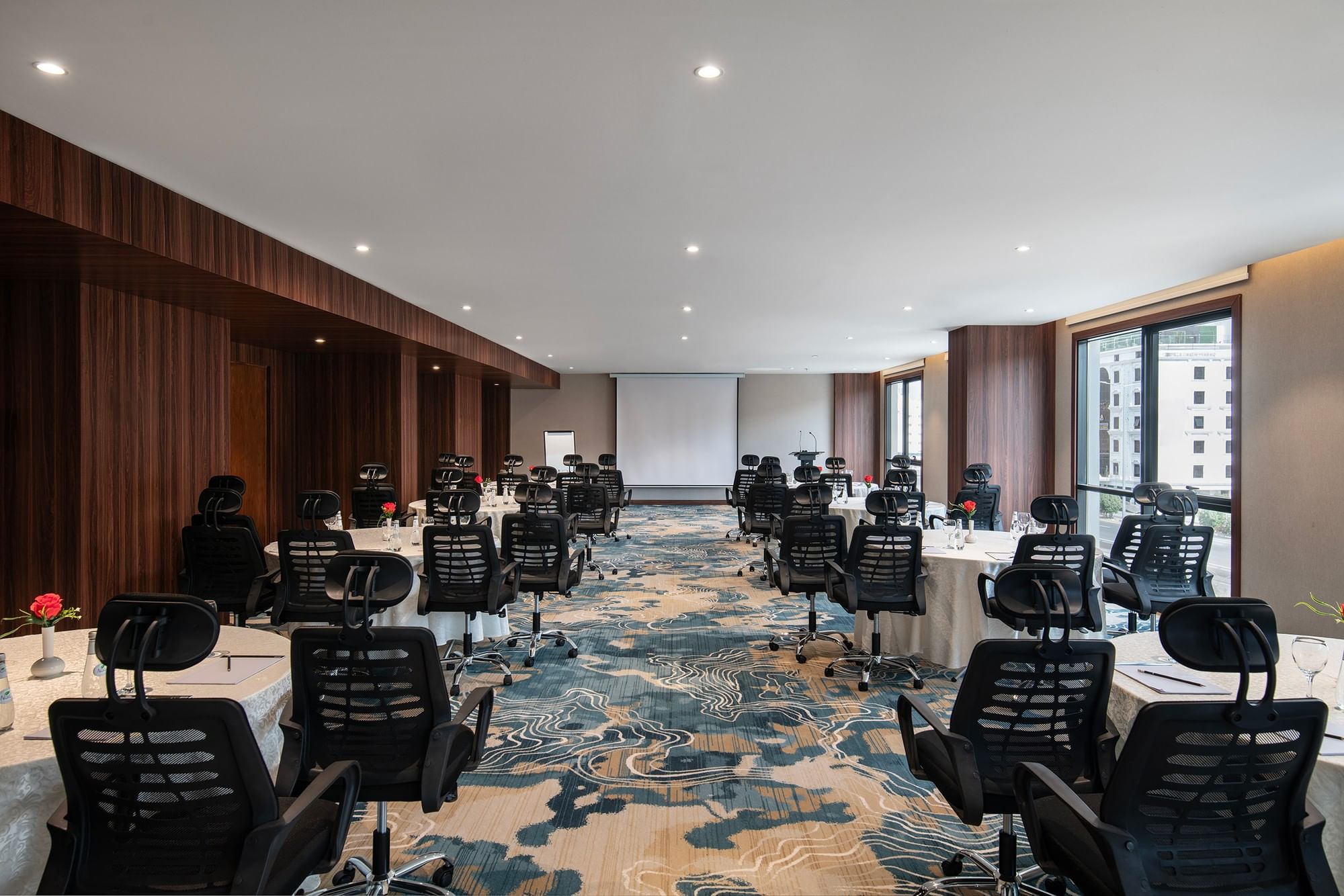 Black office chairs by round tables facing a projector screen in Amarige Hall at Warwick Hotels and Resorts