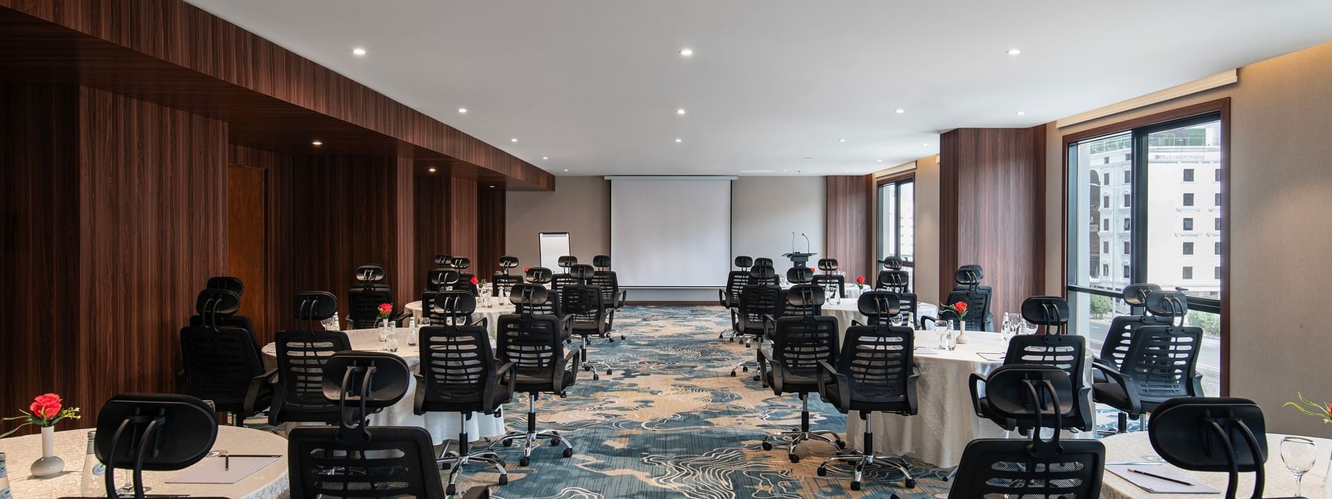 Black office chairs by round tables facing a projector screen in Amarige Hall at Warwick Hotels and Resorts