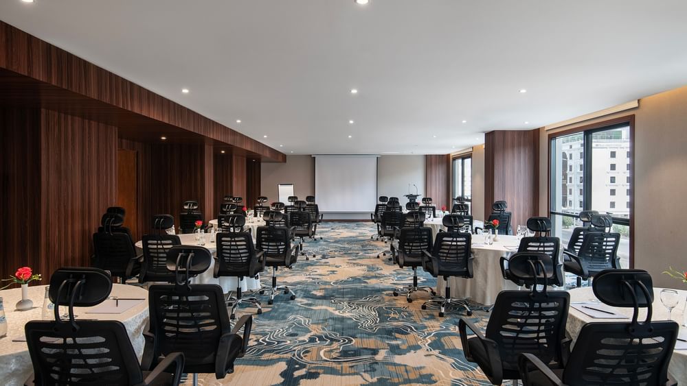 Black office chairs by round tables facing a projector screen in Amarige Hall at Warwick Hotels and Resorts