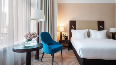 Hotel room with a double bed, blue armchair, and a vase of flowers placed at Polonia Palace Hotel