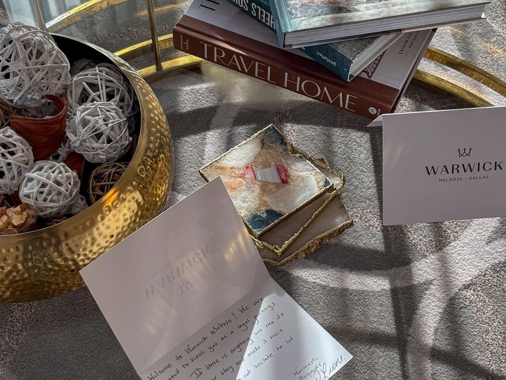 Welcome cards by a gold bowl under a stack of books on a glass table in Presidential Suite at Warwick Melrose Dallas