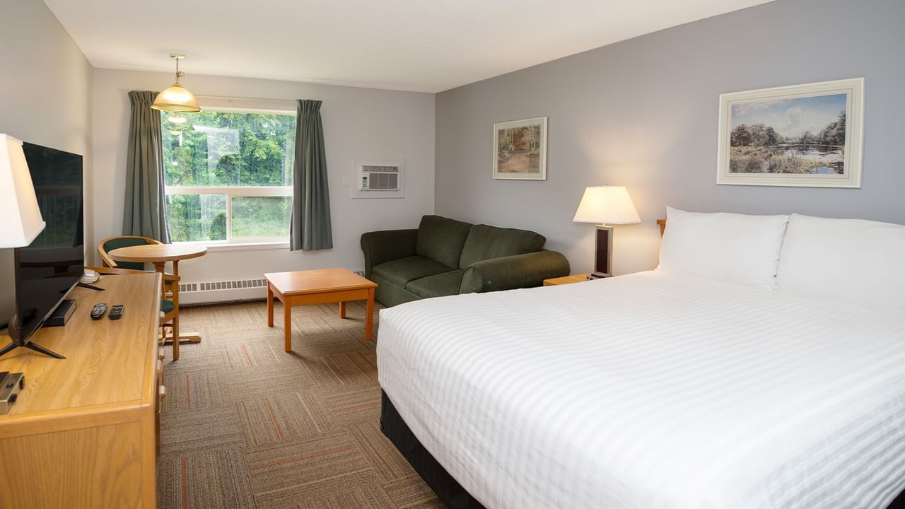 A hotel room with a bed, armchair, coffee table, TV, side table, and two framed paintings.