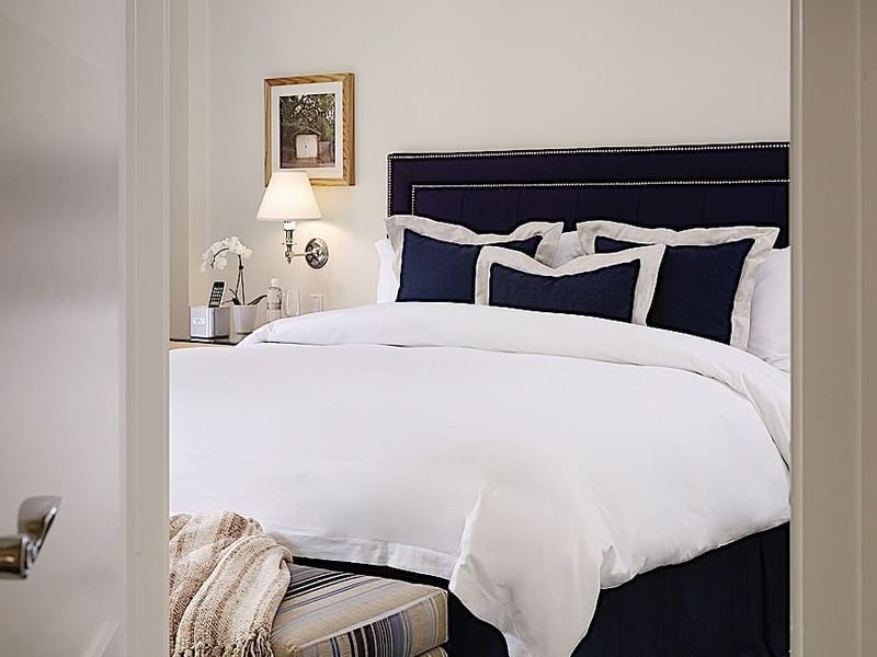 Cozy bedroom at El Prado Hotel, featuring a comfortable bed with navy accents and bedside lamp