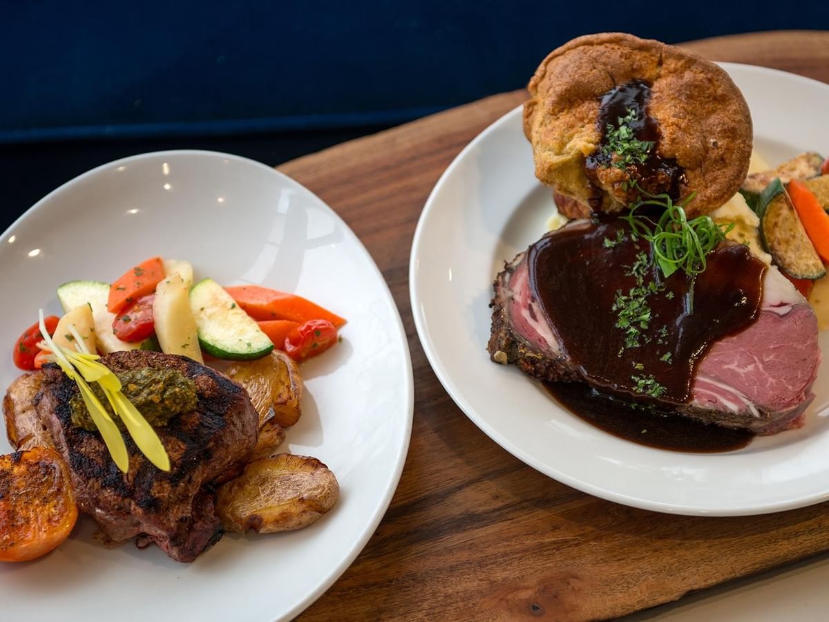 Two gourmet plates with meat, vegetables, and sauces at Minnoz Restaurant + Lounge in Nanaimo at Coast Bastion Hotel.