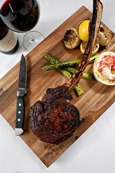 Tomahawk steak by grilled asparagus and a knife on a wooden board at The J House Greenwich